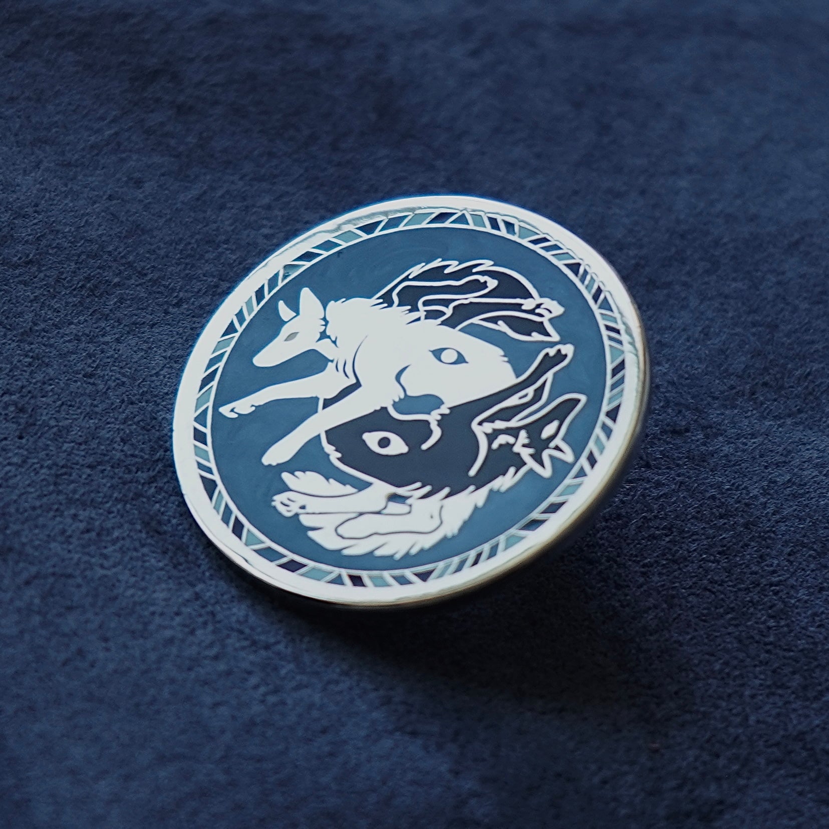 Circular emblem with a white and black wolves wolf design on a blue textured background enamel pin
